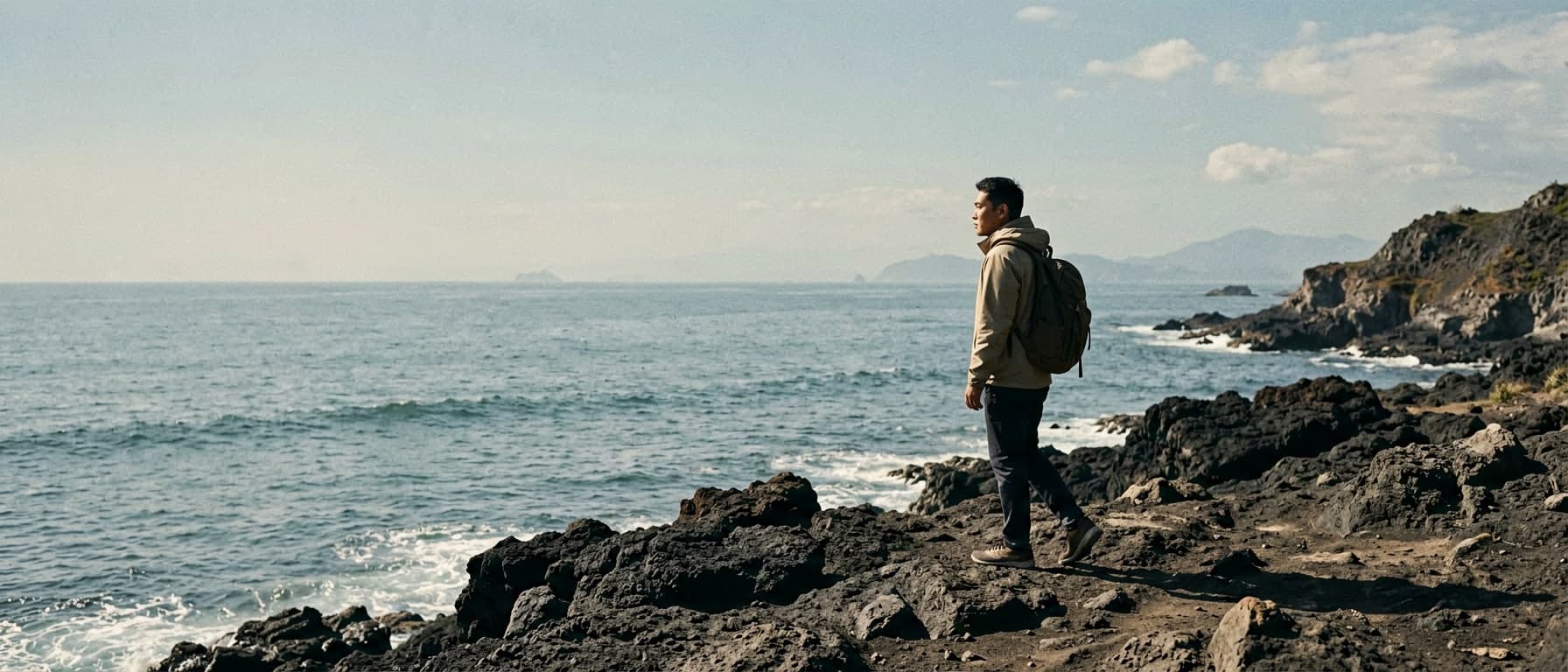 A traveler standing on a volcanic Jeju Island coast under clear daylight and open sea air.